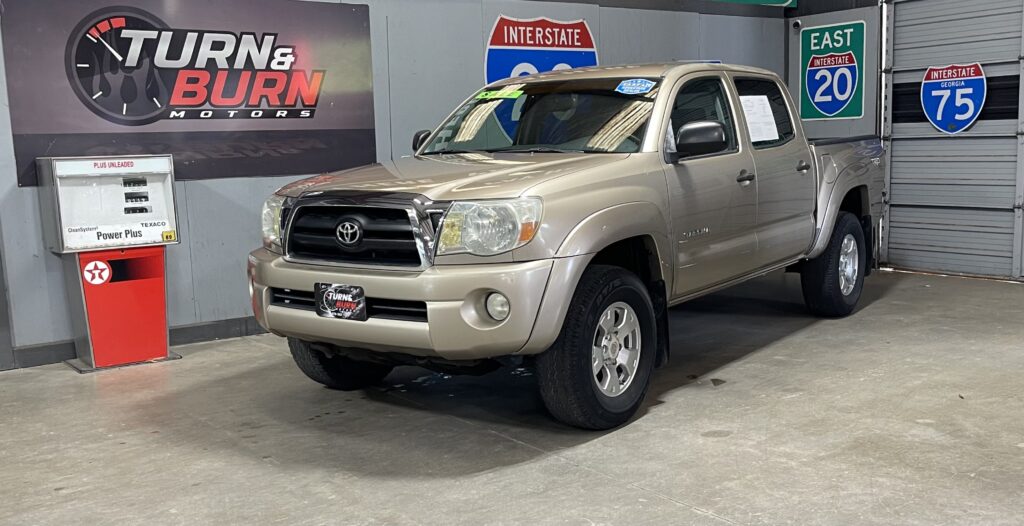 Beige Toyota Tundra pickup truck inside a showroom with Turn & Burn Motors sign and multiple Interstate road signs in the background