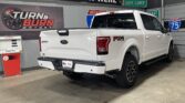 White Ford F-150 FX4 Off-Road pickup in a showroom, rear and passenger side visible with Turn & Burn Motors signage in the background.