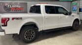 White Ford F-150 FX4 off-road pickup in a showroom, with a Turn & Burn Motors banner in the background.