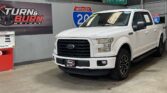 White Ford F-150 pickup on showroom floor beside dealership signage and a gas-pump display, with Turn & Burn Motors banner in the background.