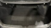 Open trunk of a dark car showing an empty cargo area with a black floor mat and trim around the opening.